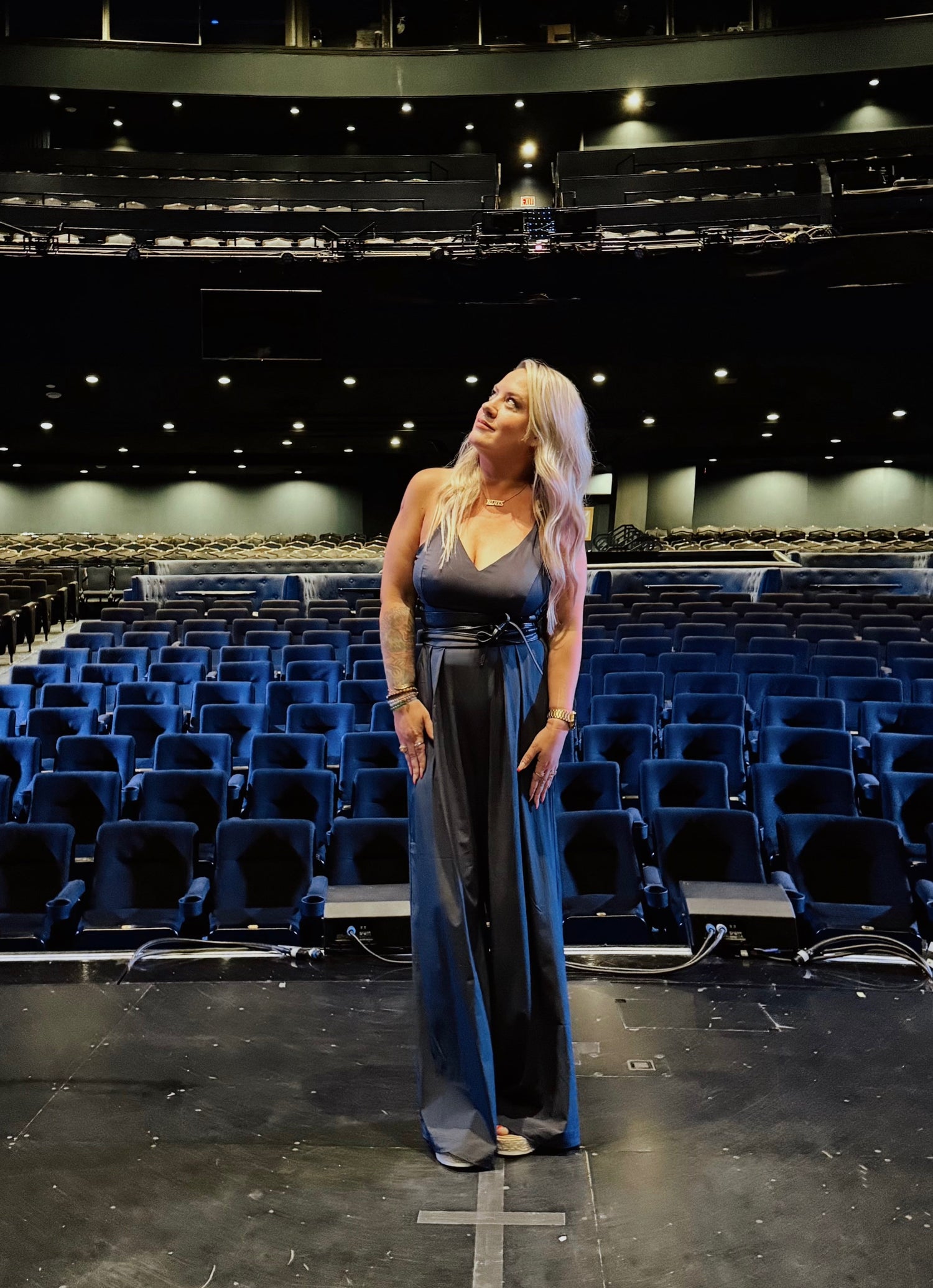 Woman in elegant black dress standing on theater stage with empty auditorium seats